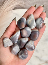 Load image into Gallery viewer, Hand holding a collection of banded agate stones with a neutral background

